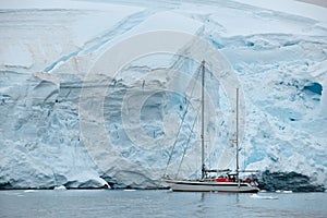 Sail boat against glacier shelf ice wall in Antarctica, Sailing ship in front of edge of glacier