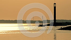 Sail boat enters a harbor at dusk near lighthouse