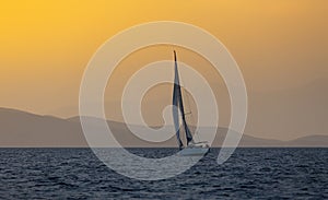 Sail boat in open sea at golden hour in evening. Mountains Silhouette in background