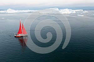 Sail boat with red sails cruising among ice bergs during dusk in front of a full moon. photo