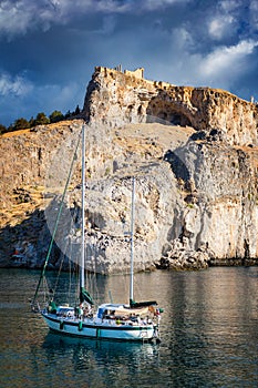 Sail boat in St. PaulÂ´s bay, cloudy blue sky, Lindos acropolis