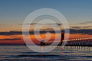 A sailboat approaches the lighthouse in Grand Haven, Michigan, at sunset on Lake Michigan