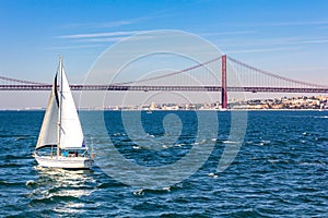 Sailboat close to April 25th Bridge over the Tagus river, Lisbon, Portugal