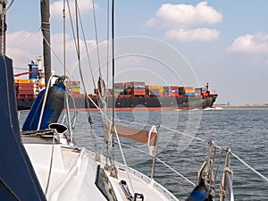 Sailboat crossing Westerschelde in the Netherlands, waiting for container ship to Antwerp, Belgium photo