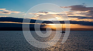 Sailboat with fallen sails in sunrise light on full sea