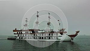 The sailboat floats on calm water, surrounded by fog