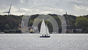 Sailboat in front of historic and modern windmills