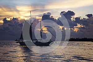 A sailboat going in front of the sunset and clouds in the ocean in Key West, Florida.