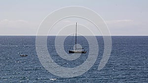 Sailboat lulled by the waves with dinghy moving away on the horizon