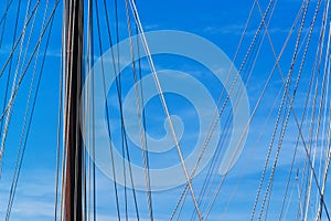 Sailboat mast and ropes in harbor against blue sky