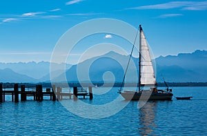 Sailboat on a quiet lake with a wooden pier and mountains in the background