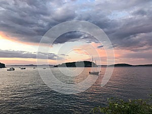 A sailboat rests in the harbor of Frenchman Bay in Bar Harbor, Maine at sunset with clouds rolling in