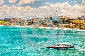 A sailboat sails in front of a Colorful hillside in Puerto Rico beach front