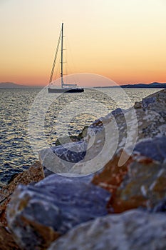 Sailboat on the sea at sunset, rocks in foreground