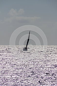 Sailboat silhouette over silver colored sea