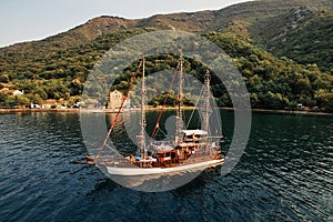 Sailboat with tourists sails along the bay against the backdrop of the mountain coast. Drone