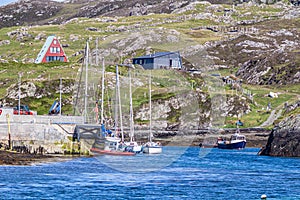 Sailboats and boats moored in the port of Inishbofin Island with a rocky hill with green grass and small houses in the background photo