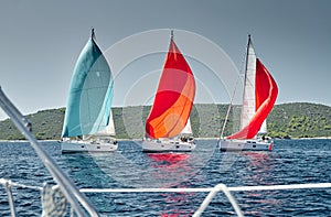 Sailboats compete in a sail regatta at sunset, view throug the ropes, race of sailboats, reflection of sails on water