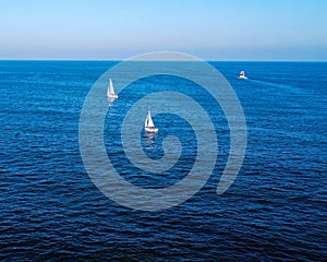 Sailboats are peacefully gliding on a tranquil, clear blue ocean under a bright sunny day