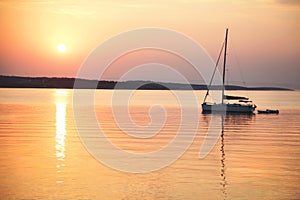 Sailing boat floats in the calm sea at sunrise