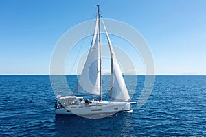 Sailing boat with open white sails, blue sky and rippled sea background