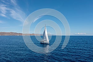 Sailing boat with open white sails, blue sky and rippled sea background