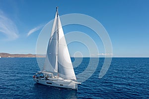 Sailing boat with open white sails, blue sky and rippled sea background