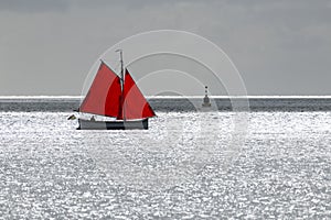 Sailing boat with red sail against the glare of the sun