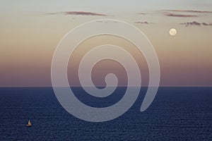 Sailing boat on the sea by moon shining in purplish sky at dusk, aerial view