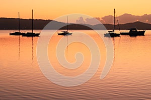 Sailing boat silhouettes in coastal landscape by golden light at dawn