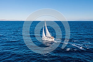 Sailing boat with white sails, cloudy sky and rippled sea background