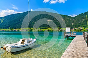 Sailing boat and wooden pier on green water Weissensee alpine lake in summer, Austria