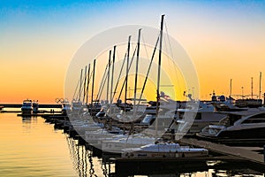 Sailing boats and luxury yachts docked in sea port in sea at sunset.