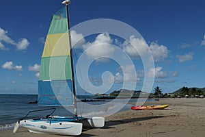 Sailing catamaran and coloured kayak on a romantic sandy beach with azure blue sea in Castries, Saint Lucia.