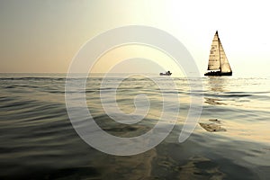 A sailing and a fishing boat on the horizon in the middle of the sea when the sun goes down at the misty day. photo