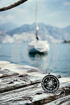 Sailing: nautical compass on wooden dock pier. Sailing boats in the background