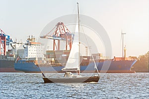 Sailing ship on the Elbe river in Hamburg in front of container ship and harbor in the evening sun
