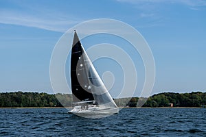 Sailing ship yacht with white and black sails in the Sea or lake.