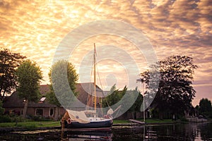A sailing traditional dutch boat anchored in a canal outside a house with golden cloudy sky, Holland. photo