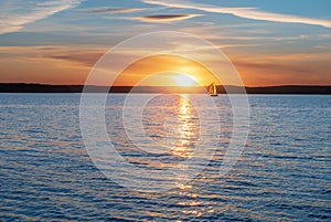 A sailing yacht against the background of the setting sun. Calming water evening landscape