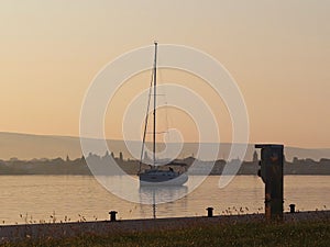 The sailing yacht enters under the motor in the marina in the rays of the morning sun. Dawn in the port. Empty pier with