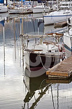 Sailing yacht with folded mast and cabins moored to the pier next to other yachts in the harbor