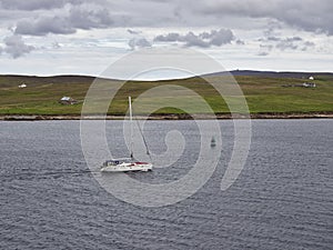 A Sailing Yacht with its sail stowed motors towards the Town of Lerwick with Bressay in the background. .