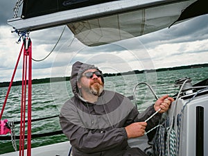 Sailing on a yacht in rainy weather. adult man using a winch to pull a rope on a sailboat or sailing yacht to control a yacht sail