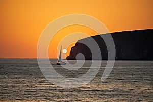 sailing yacht rounding headland, with the sun setting in the background