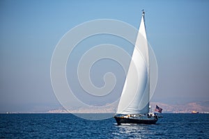 Sailing yacht with white sails in the fog in the sea near the coast. Luxury.