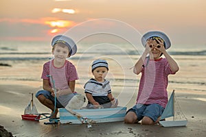 Sailor baby boy, cute child, playing on the beach with wooden bo