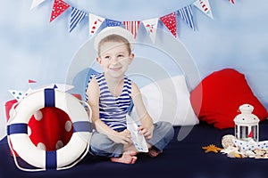 Sailor boy sitting with stearing wheel in marine decor