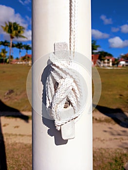 Sailor knot on white wooden post and French West Indies background. Close-up of white navigation rope. Cordage and nautical