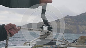 Sailor man reel up rope on board sailing yacht closeup. Yachtsman works with rope